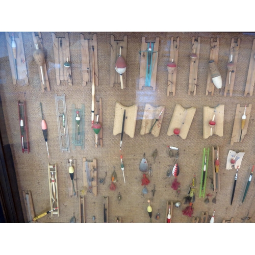 1223 - A collection of fishing floats, trout flies, and lures mounted in a glazed display case. 90 x 90cm.