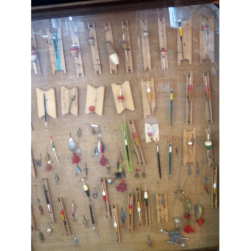 1223 - A collection of fishing floats, trout flies, and lures mounted in a glazed display case. 90 x 90cm.