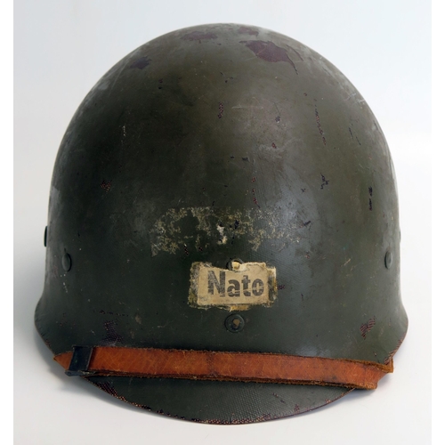 1384 - An American M1 pattern helmet liner with leather chin strap, bears paper label 'NATO' to the front.