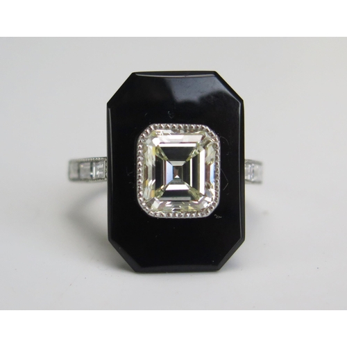 An Emerald Cut Diamond and Onyx Ring in a platinum setting with three baguette cut diamonds to each shoulder and in a John Hall & Co. of Manchester contemporary box. The principal stone estimated at 2.2ct, K colour and VS or better, 19.5x13.5mm head, 7.08g