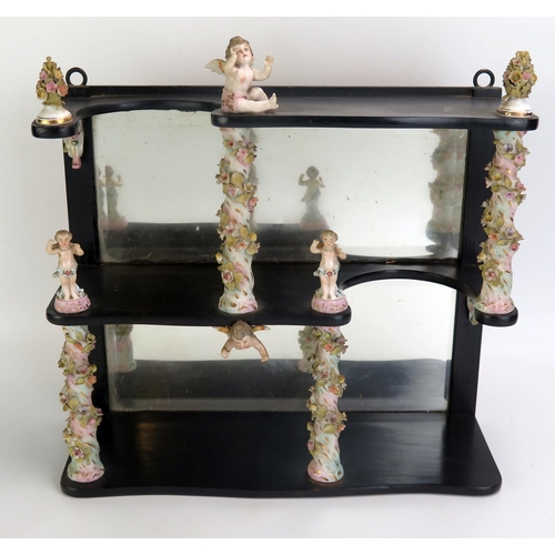 1061 - A 19th century ebonised and porcelain set of shelves with mirror panelled back, the porcelain column... 