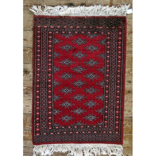 1567 - A Turkoman rug, the wine red field with rows of hooked lozenge medallions, enclosed by a triple geom... 