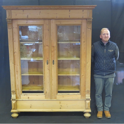 1602 - A large Victorian stripped pine bookcase, with a moulded cornice above a pair of glazed panelled doo... 