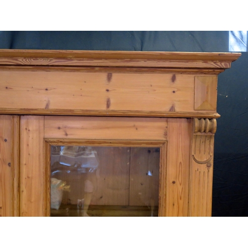 1602 - A large Victorian stripped pine bookcase, with a moulded cornice above a pair of glazed panelled doo... 