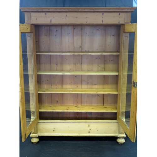 1602 - A large Victorian stripped pine bookcase, with a moulded cornice above a pair of glazed panelled doo... 