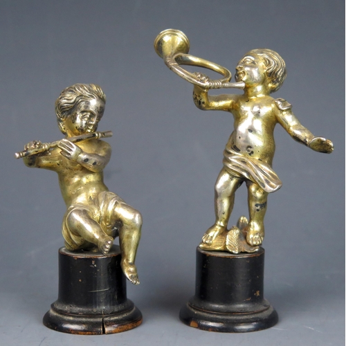 718 - A pair of continental silver gilt putti one playing a flute the other blowing a horn, mounted on ebo... 