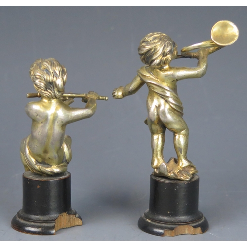 718 - A pair of continental silver gilt putti one playing a flute the other blowing a horn, mounted on ebo... 