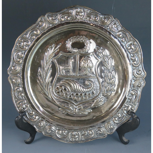 728 - A Peruvian silver platter, stamped 925, with embossed armorial decorated centre enclosed by a foliat... 