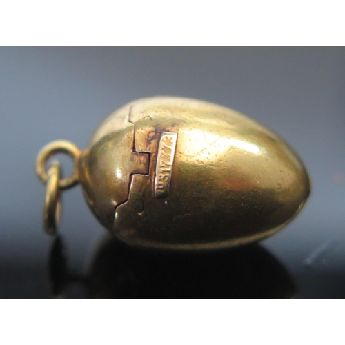 296 - A Precious Yellow Metal Articulated Egg Pendant with spring loaded mechanism opening to reveal a chi... 