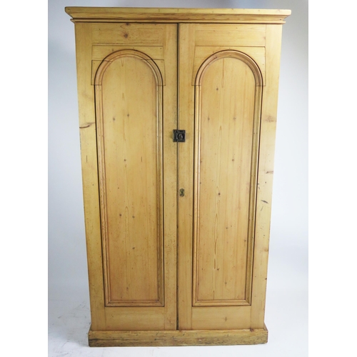 1707 - A Victorian stripped pine cupboard, the top with a moulded cornice above a pair of arched moulded pa... 