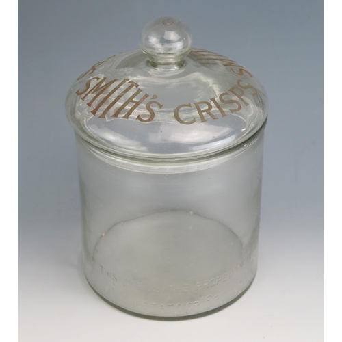 173 - A clear glass advertising jar and cover for 'Smiths Crisps' of cylindrical outline, with domed cover... 