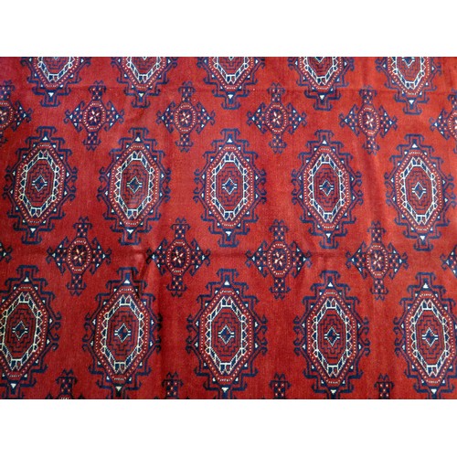 1684 - A Turkomen carpet, the wine red field with four rows of lozenge medallions, enclosed in a multiple g... 