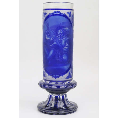 1184 - A Bohemian overlay blue glass vase, of cylindrical form, the central panel depicting drinking cavali... 