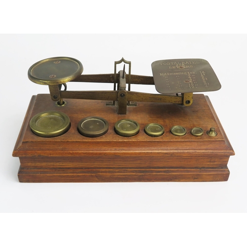 1264 - A set of brass postage balance scales, mounted on an oak base with graduated brass weights.