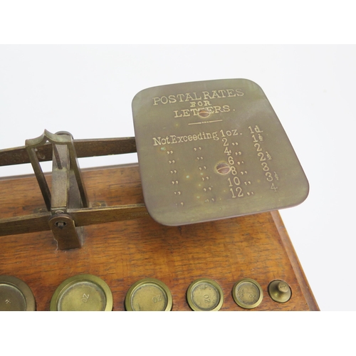 1264 - A set of brass postage balance scales, mounted on an oak base with graduated brass weights.