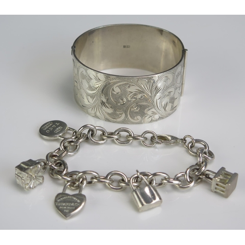 280 - A Silver Hinged Bangle with chased foliate decoration and a Tiffany silver charm bracelet, 11.92g