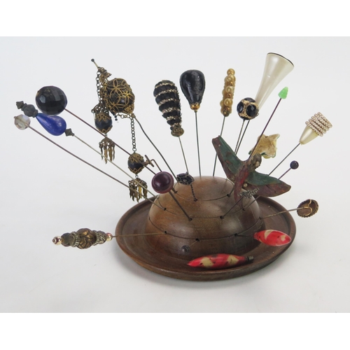 1274 - A collection of Victorian and later hat pins, mounted in a turned wood hat pin holder.