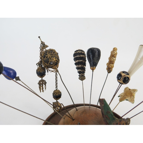 1274 - A collection of Victorian and later hat pins, mounted in a turned wood hat pin holder.