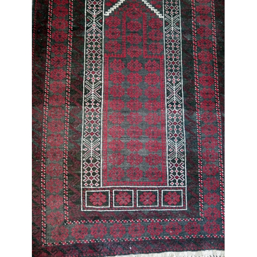 1396 - An Afghan baluch prayer rug, the wine red field with hooked and stepped mirab, enclosed by a triple ... 