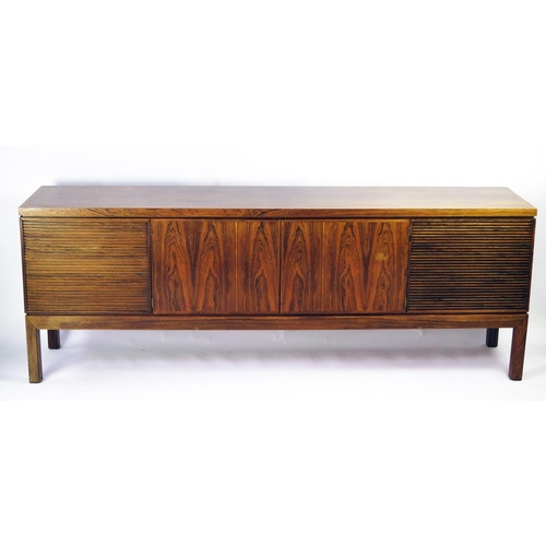 1464 - A modernist rosewood sideboard of rectangular outline, containing a pair of plain field central cupb... 