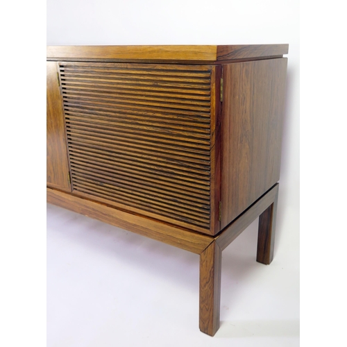 1464 - A modernist rosewood sideboard of rectangular outline, containing a pair of plain field central cupb... 