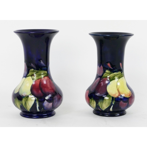 1711 - A pair of Moorcroft pottery vases with Wisteria pattern decoration, on a blue ground, 18cm high, (2)... 