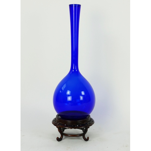 1715 - A tall blue glass vase, of ovoid form with long slender neck, on an associated Chinese hardwood stan... 