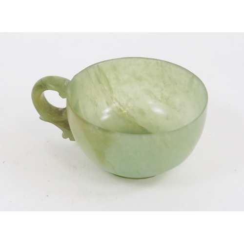 1771 - A Chinese carved jade cup, with pierced scroll handle on a circular foot, 8cm wide.