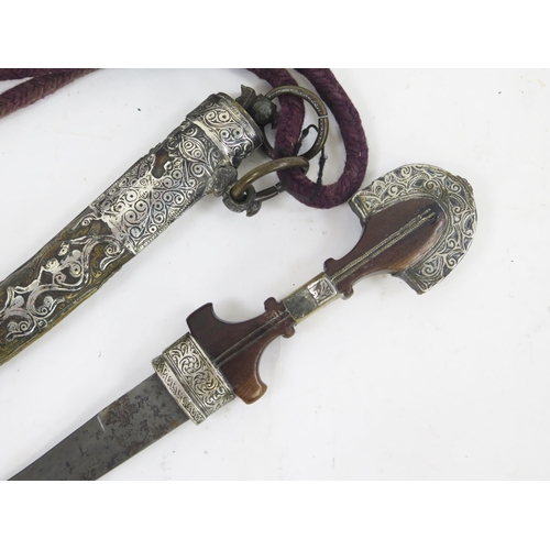 1829 - An Indo-Persian jambiya, with 24cm curved blade, with wooden and brass grip contained in a silver an... 