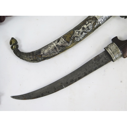 1829 - An Indo-Persian jambiya, with 24cm curved blade, with wooden and brass grip contained in a silver an... 