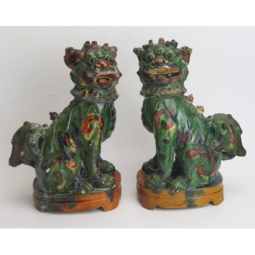 1184A - A pair of Chinese pottery models of temple dogs, with green and orange ochre glaze, raised on oval b... 