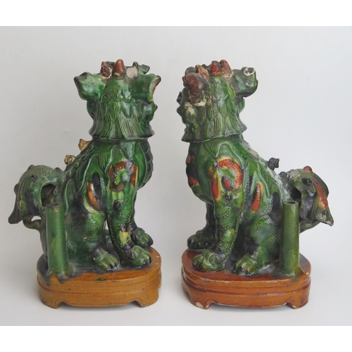 1184A - A pair of Chinese pottery models of temple dogs, with green and orange ochre glaze, raised on oval b... 