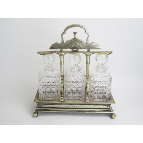 588 - A late Victorian/Edwardian plated tantalus containing three clear glass decanters and stoppers, of r... 