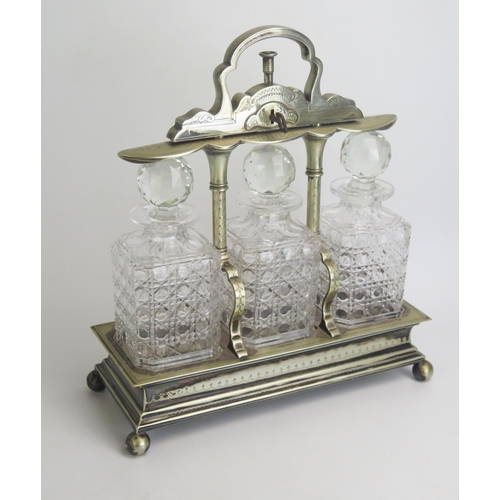 588 - A late Victorian/Edwardian plated tantalus containing three clear glass decanters and stoppers, of r... 