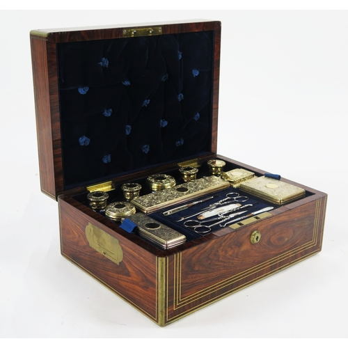 A George IV rosewood and brass strung travelling vanity box, of rectangular form the hinged lid with mirror panel to the inner side, enclosing an arrangement of clear glass and silver gilt mounted jars and bottles, maker TD possibly Thomas Dick, London, 1825, with lift-out tray containing MOP and gold handled manicure set, weighable silver 317gms, 10.20ozst, 33cm wide, 15.5cm high, 25cm deep.