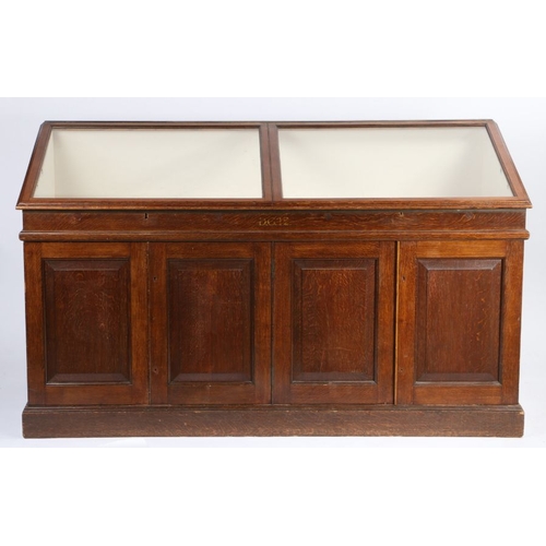 1 - Oak museum display cabinet, the sloping hinged glazed top above four cupboard doors, raised on a pli... 