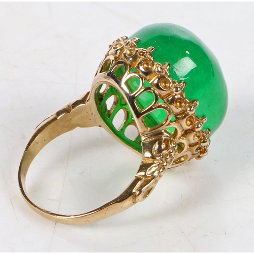 71 - An impressive jade and yellow metal ring, the head set with a large claw mounted cabochon cut jade s... 