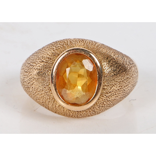 92 - An 18 carat gold and citrine ring, the oval facet cut citrine housed in a beaten effect mount, ring ... 