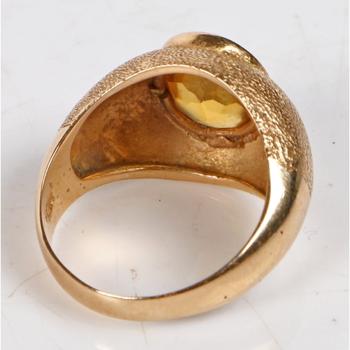 92 - An 18 carat gold and citrine ring, the oval facet cut citrine housed in a beaten effect mount, ring ... 