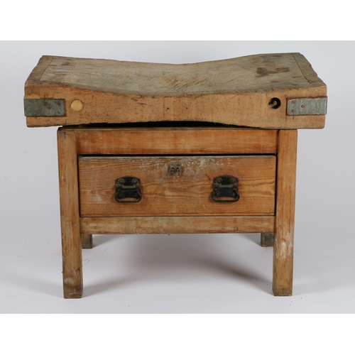 60 - A PINE BUTCHERS BLOCK. The well used block top with metal corner brackets, above a base with single ... 