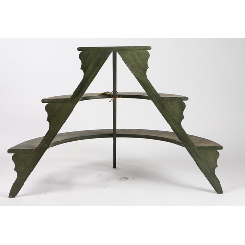 70 - A DEMI-LUNE THREE TIER PLANT STAND. with three graduated dark green painted shelves on silhouette su... 