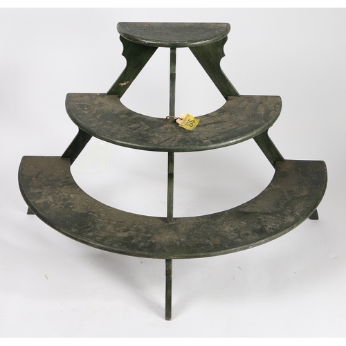 70 - A DEMI-LUNE THREE TIER PLANT STAND. with three graduated dark green painted shelves on silhouette su... 