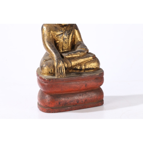 78 - A CARVED AND GILT WOOD BUDDHA. modelled in a seated position and raised on a red painted plinth base... 