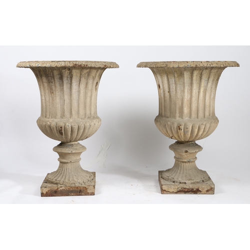 85 - A PAIR OF CAST IRON GARDEN URNS. of classical form with reeded bodies and stems, raised on square pl... 