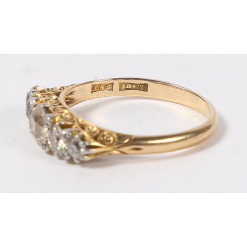 14 - AN 18 CARAT GOLD AND DIAMOND RING. the pierced scroll engraved head set with five graduated round cu... 