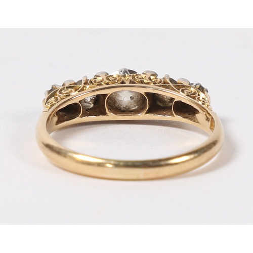 14 - AN 18 CARAT GOLD AND DIAMOND RING. the pierced scroll engraved head set with five graduated round cu... 