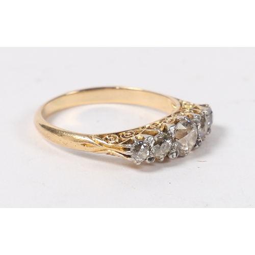 14 - AN 18 CARAT GOLD AND DIAMOND RING. the pierced scroll engraved head set with five graduated round cu... 