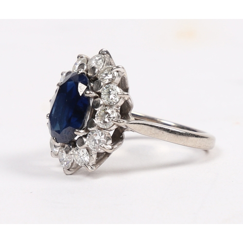 25 - AN 18 CARAT WHITE GOLD, SAPPHIRE AND DIAMOND CLUSTER RING. the central oval face cut sapphire surrou... 