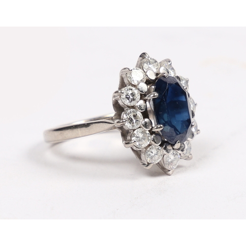 25 - AN 18 CARAT WHITE GOLD, SAPPHIRE AND DIAMOND CLUSTER RING. the central oval face cut sapphire surrou... 