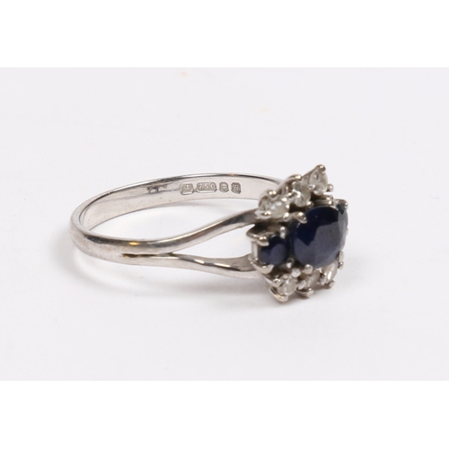 32 - AN 18 CARAT WHITE GOLD SAPPHIRE AND DIAMOND RING. the central oval facet cut sapphire flanked by two... 